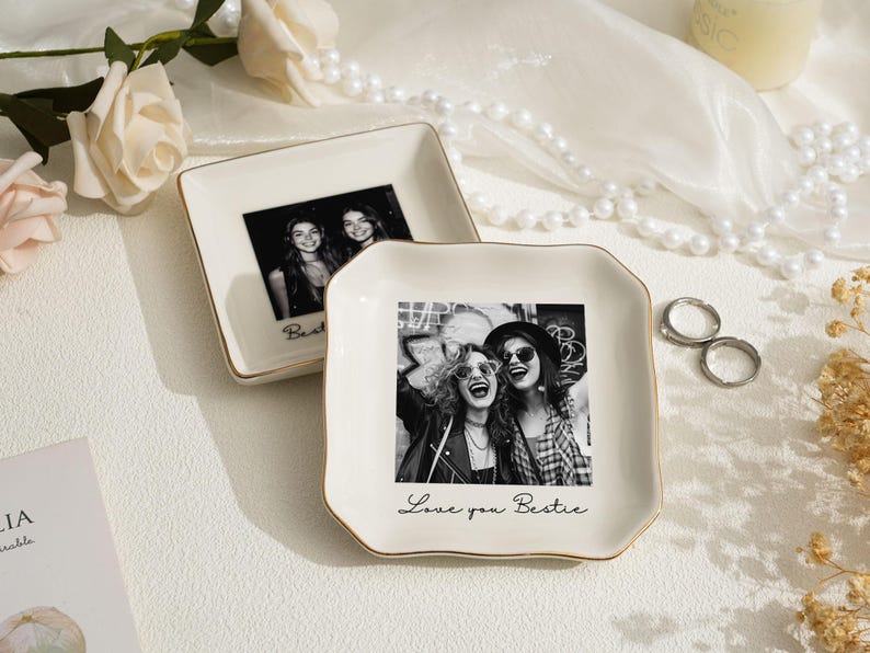 May include: Two off-white ceramic trinket dishes with gold trim. Each dish features a black and white photograph of two people. One dish has the word "Bestie" and the other says "Love you Bestie".