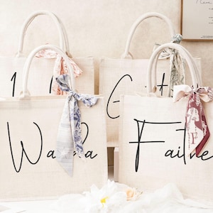 May include: Four white canvas tote bags with black script lettering. The bags are decorated with fabric ribbons in various colors and patterns. The bags are labeled "1", "G", "Wanda", and "Faith".