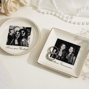 May include: Two ceramic trinket dishes with gold trim. One is round, the other square. Each features a black and white photo of smiling women. The round dish says "Love you Bestie", the square dish says "Bestie Forever".