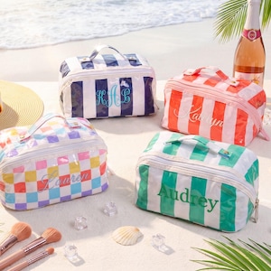 May include: Four personalized cosmetic bags in various colors and patterns, including blue and white stripes, pink and white stripes, a colorful checkerboard, and green and white stripes. Each bag has a handle and a name embroidered on it.