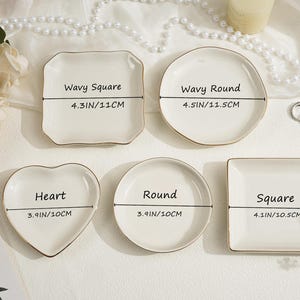 May include: A collection of small, white ceramic dishes in various shapes: wavy square (4.3 inches/11 cm), wavy round (4.5 inches/11.5 cm), heart (3.9 inches/10 cm), round (3.9 inches/10 cm), and square (4.1 inches/10.5 cm). Each dish has a gold rim.