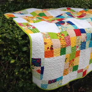 May include: A patchwork quilt with a white background and squares of various colors, including red, orange, yellow, green, blue, and purple. The quilt is made of different fabrics with floral and geometric patterns.