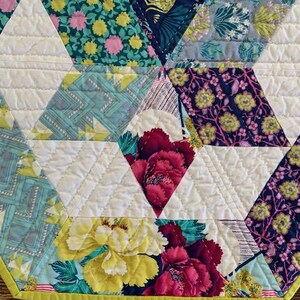 May include: A close-up of a quilt with a geometric pattern of triangles. The quilt is made of various fabrics with floral and geometric designs in shades of blue, green, pink, yellow, and white. The quilt is edged with a bright yellow trim.