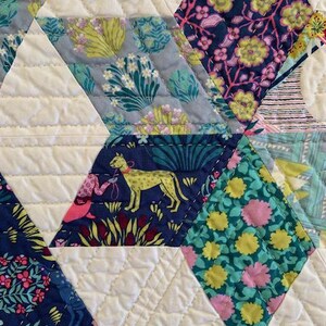 May include: A close-up of a quilt with a diamond pattern. The quilt is made of different fabrics with floral and animal prints. The fabric colors are blue, green, pink, yellow, and white.