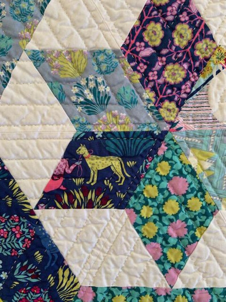 May include: A close-up of a quilt with a diamond pattern. The quilt is made of different fabrics with floral and animal prints. The fabric colors are blue, green, pink, yellow, and white.