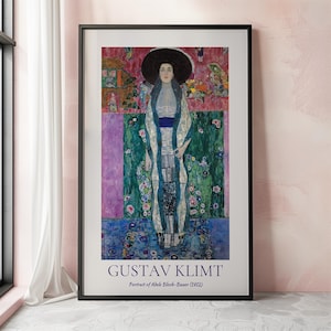 May include: A framed poster of a painting by Gustav Klimt titled "Portrait of Adele Bloch-Bauer (1912)". The painting features a woman in a white dress with a blue sash, standing against a background of green, pink, and gold.