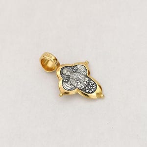以下が含まれることがあります： 翼のある天使の宗教的な画像が描かれた金と銀のペンダント。ペンダントは十字架の形をしており、チェーンに取り付けるためのループが上部に付いています。