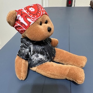 May include: A brown teddy bear wearing a red bandana with white polka dots and a black denim jacket.