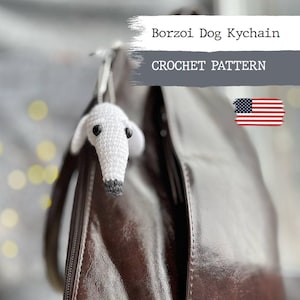 May include: White crocheted Borzoi dog keychain hanging on a brown leather bag. The keychain is a crochet pattern and the image includes the text "Borzoi Dog Keychain" and "CROCHET PATTERN".