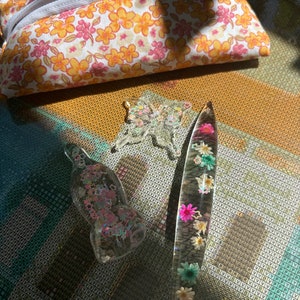 Peut inclure: Trois objets en résine transparente avec des fleurs pressées et des paillettes. Un papillon, une baguette fine et longue et une petite forme ronde et bulbeuse.