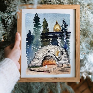 May include: Watercolor painting in a wooden frame. The artwork depicts a stone structure with an arched entrance, a golden dome, and tall trees. The color palette includes blues, greens, and browns, creating a serene landscape scene.