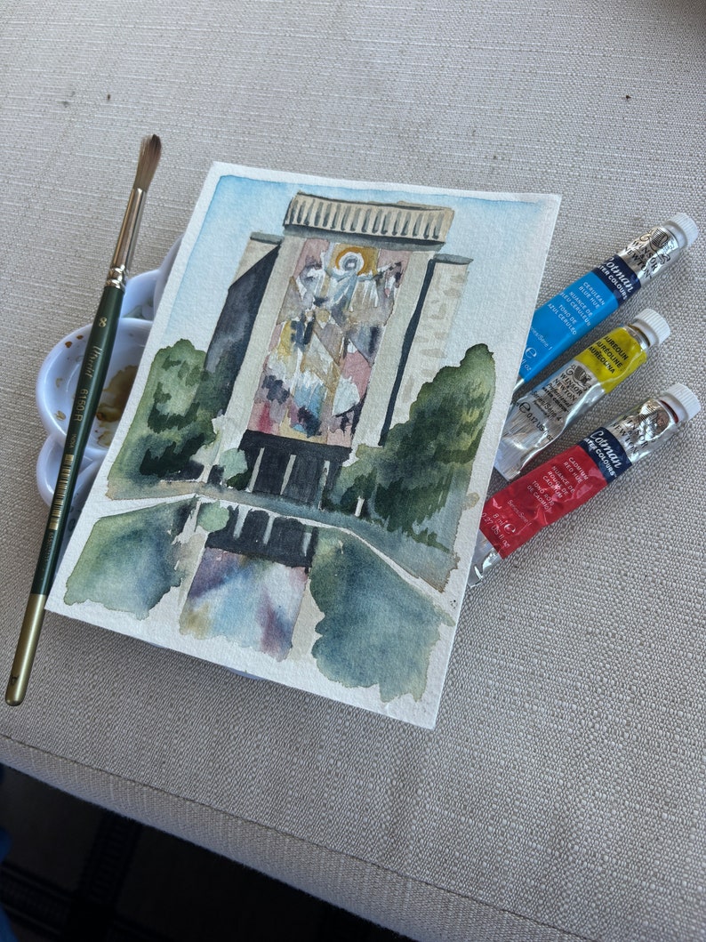 May include: Watercolor painting of a building with a large mural on the side. The mural depicts a religious scene with figures in white and gold. The painting is on a white background and is surrounded by green trees.