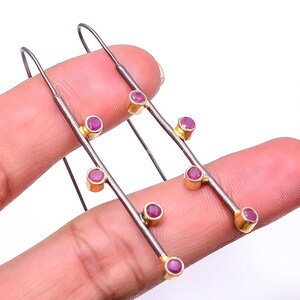 May include: A pair of long drop earrings featuring dark oxidized silver bars accented with small, round, bezel-set pink gemstones. Each earring has a gold-toned metal setting for the stones and a simple hook wire for attachment to the earlobe.