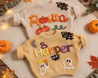 May include: Two long-sleeve knit sweaters featuring Halloween-themed embroidery. The top sweater is beige with the name Rosita and orange pumpkin designs. The bottom sweater is yellow with the name Harper, a spider, ghosts, and a web.