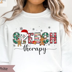 May include: White Christmas-themed sweatshirt with the words "Speech Therapy" in a festive font. The letters are decorated with gingerbread men, reindeer, and Christmas trees.