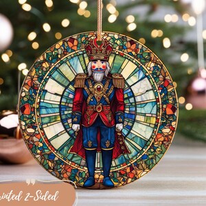May include: A round, glass Christmas ornament featuring a colorful stained glass design of a Nutcracker soldier. The ornament is printed on both sides and has a gold string for hanging.