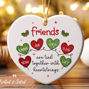 May include: White heart-shaped ceramic ornament with the text "Friends are tied together with heartstrings" and six smaller hearts with names printed on them. The ornament is decorated with red and green holly leaves and red stars.