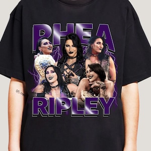 Puede incluir: Camiseta negra con un gr&aacute;fico morado de Rhea Ripley y el texto "RHEA RIPLEY". El dise&ntilde;o presenta m&uacute;ltiples im&aacute;genes de Rhea Ripley con un efecto de rayo, creando un impacto visual llamativo.
