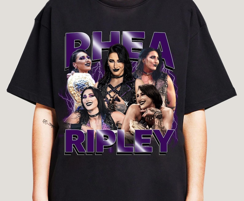 Puede incluir: Camiseta negra con un gr&aacute;fico morado de Rhea Ripley y el texto "RHEA RIPLEY". El dise&ntilde;o presenta m&uacute;ltiples im&aacute;genes de Rhea Ripley con un efecto de rayo, creando un impacto visual llamativo.