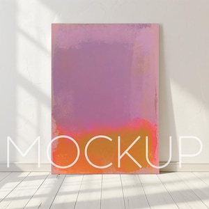 Puede incluir: Un lienzo rectangular con un diseño abstracto mezclado en tonos de morado, rosa y naranja. La palabra "MOCKUP" está escrita en letras blancas estilizadas en la parte inferior del lienzo. El lienzo está apoyado contra una pared blanca.