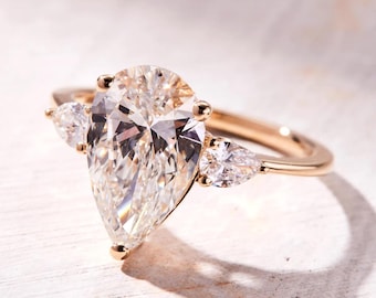 May include: A pear-shaped diamond engagement ring with two smaller pear-shaped diamonds on the band. The ring is set in gold.