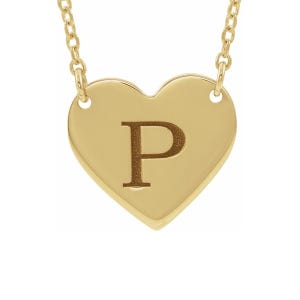 May include: A gold-toned heart-shaped pendant necklace featuring the letter P engraved in the center. The pendant is suspended from a delicate gold-toned chain that attaches to the top of the heart on both sides.
