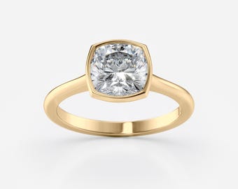 Könnte beinhalten: Ein goldener Ring mit einem quadratischen Kissenschliff-Diamanten. Der Diamant ist in einer Lünettenfassung gefasst, und das Band ist ein schlichtes, poliertes Gold. Der Ring wird vor einem weißen Hintergrund gezeigt.