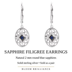 May include: A pair of sterling silver earrings featuring an oval filigree design with a central 2 mm round blue sapphire. The text SAPPHIRE FILIGREE EARRINGS, Natural 2 mm round blue sapphires, Solid sterling silver, Sold as a pair, and BLOOM BRILLIANCE is visible.