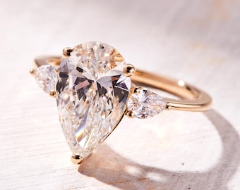 May include: A pear-shaped diamond engagement ring set in gold with two smaller pear-shaped diamonds on either side.