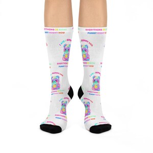 May include: White socks featuring a colourful gummy bear design and the text "I ate a gummy and everything is extra funny right now." The socks have black heels and toes.