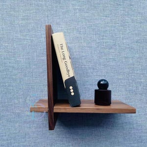 Peut inclure: Une étagère en bois avec un livre intitulé "The Long Goodbye" et une bouteille noire avec un dessus rond.