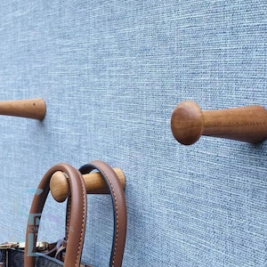May include: Wooden wall hooks with a rounded knob design. The hooks are made of light brown wood and are mounted on a textured blue wall. A brown leather handbag hangs from one of the hooks.