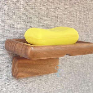May include: A wooden soap dish with a yellow bar of soap. The dish is made of dark wood and has a simple design.