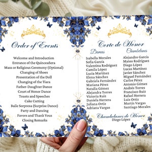 Pode incluir: Um cartão branco com bordas florais douradas e azuis e uma coroa dourada. O cartão lista a ordem dos eventos para uma celebração de Quinceañera, incluindo a entrada da Quinceañera, a troca de sapatos, a apresentação da boneca e a dança de pai e filha. Também lista os nomes da Corte de Honra, incluindo as damas e os chambelanes.