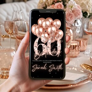 May include: A smartphone displays a 60th birthday invitation. The design features rose gold balloons, the number 60, and the words "Birthday" and "Sarah Smith" on a black background. The invitation is held in a person's hand.