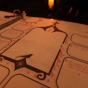 May include: Open journal with a decorative design featuring a bird silhouette and ornate shapes. The pages have pre-printed prompts and spaces for writing. The journal is open, revealing the interior pages and a binder ring.