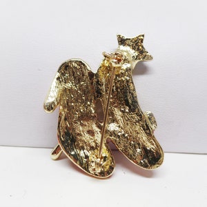Puede incluir: Broche dorada con un dise&ntilde;o estilizado de dos p&aacute;jaros con piedras de imitaci&oacute;n rojas y transparentes. La broche tiene un cierre de pin.