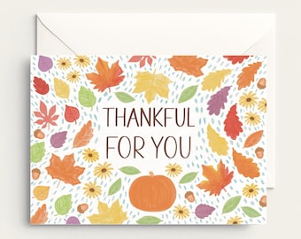 May include: A greeting card with the text "THANKFUL FOR YOU" surrounded by colorful autumn leaves, flowers, acorns, and a pumpkin. The card is paired with a white envelope, perfect for sending a seasonal message.