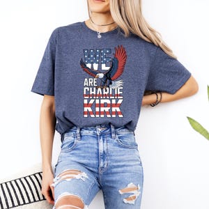 Puede incluir: Una camiseta azul marino con un gr&aacute;fico de un &aacute;guila con alas rojas, blancas y azules y el texto "WE ARE CHARLIE KIRK". La camiseta est&aacute; hecha de un material suave y es adecuada para ropa casual.