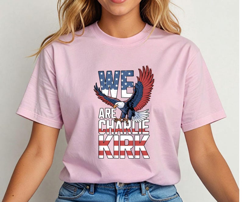 Puede incluir: Camiseta rosa claro con un &aacute;guila calva americana con las alas extendidas. El texto "WE ARE CHARLIE KIRK" se muestra en rojo, blanco y azul, reflejando la bandera estadounidense. La camiseta es de estilo cuello redondo cl&aacute;sico.