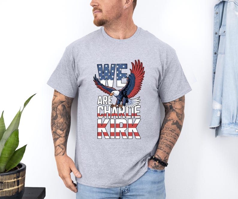 Puede incluir: Camiseta gris claro con un &aacute;guila de alas rojas, blancas y azules y el texto "WE ARE CHARLIE KIRK". El &aacute;guila est&aacute; sobre el texto, que est&aacute; dise&ntilde;ado para parecerse a la bandera estadounidense.