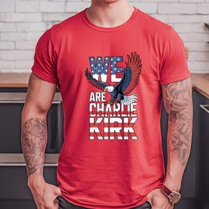 Puede incluir: Camiseta roja con un &aacute;guila calva americana y el texto "WE ARE CHARLIE KIRK". Las palabras son en blanco y azul, con la palabra "WE" dise&ntilde;ada con estrellas y rayas, que recuerdan la bandera estadounidense.