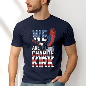 Puede incluir: Camiseta azul marino con un &aacute;guila calva americana y el texto "WE ARE CHARLIE KIRK". El texto incorpora los colores de la bandera estadounidense. Las alas del &aacute;guila son rojas y azules.