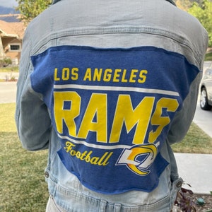 Puede incluir: Una chaqueta vaquera azul claro con un parche de fútbol de los Los Angeles Rams azul y amarillo cosido en la espalda.
