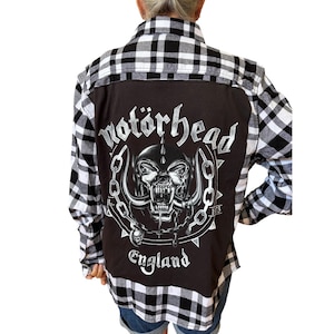 May include: A long-sleeve button-down shirt featuring a black and white plaid pattern on the sleeves and collar, with a large black panel on the back. The back displays a white graphic of a skull with horns, chains, and the text Motörhead England.