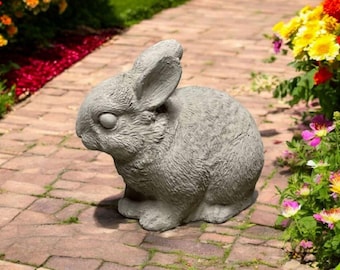 May include: A gray concrete rabbit statue with a detailed, realistic design. The rabbit is sitting on a brick pathway with flowers in the background.