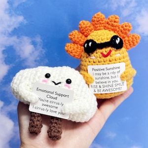 Puede incluir: Una nube blanca de crochet con una cara sonriente sostiene un cartel que dice "Emotional Support Cloud You're cirrus-ly awesome I cirrus-ly love you!"  Un sol amarillo de crochet con una cara sonriente y gafas de sol sostiene un cartel que dice "Positive Sunshine I may be a rdy of sunshine, but I believe in you. RISE & SHINE SMILE & BE AWESOME!"