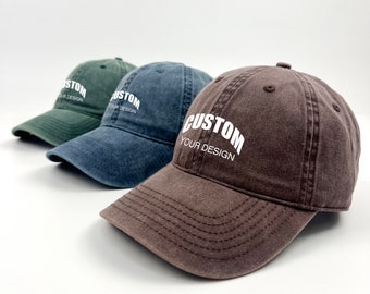 Op de afbeelding: Drie baseballpetten op een rij, elk met een gebogen klep en verstelbare band. De petten zijn in groen, blauw en bruin. Elke pet heeft het woord "CUSTOM" boven "YOUR DESIGN" in witte letters.