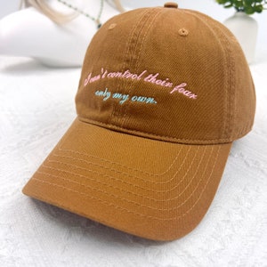 May include: A brown baseball cap with the embroidered text "I can't control their fear only my own" in pink and light blue. The cap has a curved brim and a stitched design.