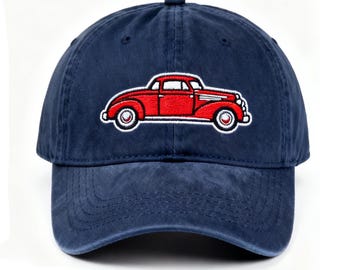 Puede incluir: Gorra de béisbol azul marino con un coche clásico rojo bordado en la parte delantera. El coche tiene detalles blancos y está sobre un fondo blanco. La gorra está hecha de un material suave y duradero.